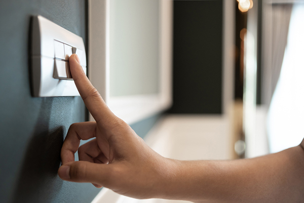 Closeup of Asian woman hand is turning on or off on grey light switch over green wall in the hotel. Copy space. Energy saving.